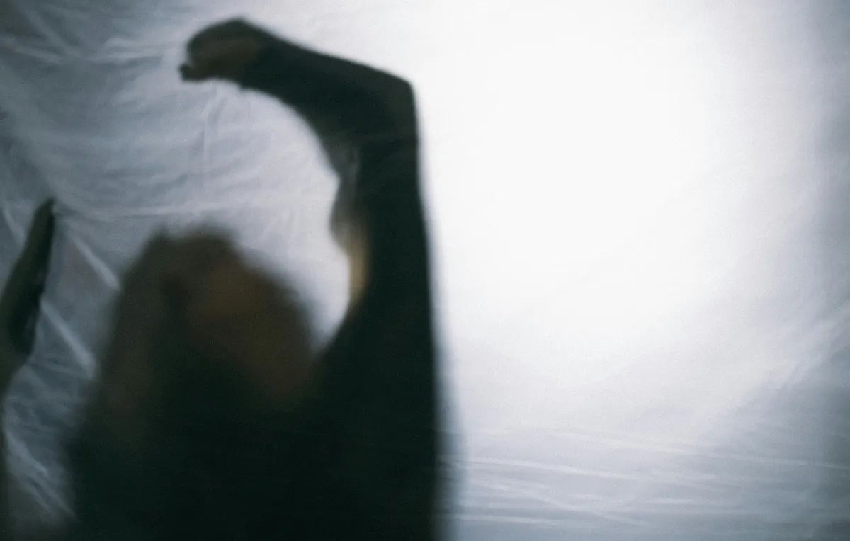 Blurred silhouette of a person trapped behind a translucent plastic sheet with a raised fist, symbolising the fear, helplessness and invisible pain of emotional abuse
