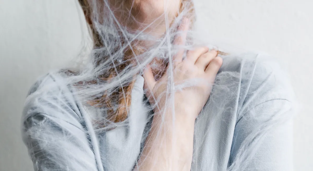Woman entangled in white threads symbolising the feeling of being trapped and overwhelmed by anxiety, stress or mental health struggles