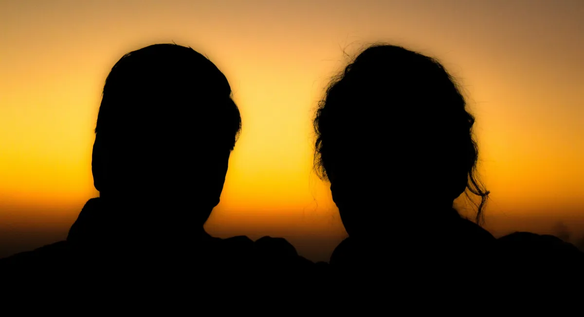 Silhouettes of a couple sitting side by side against a warm sunset, symbolising distance, communication difficulties and relationship challenges in couples therapy in Denmark