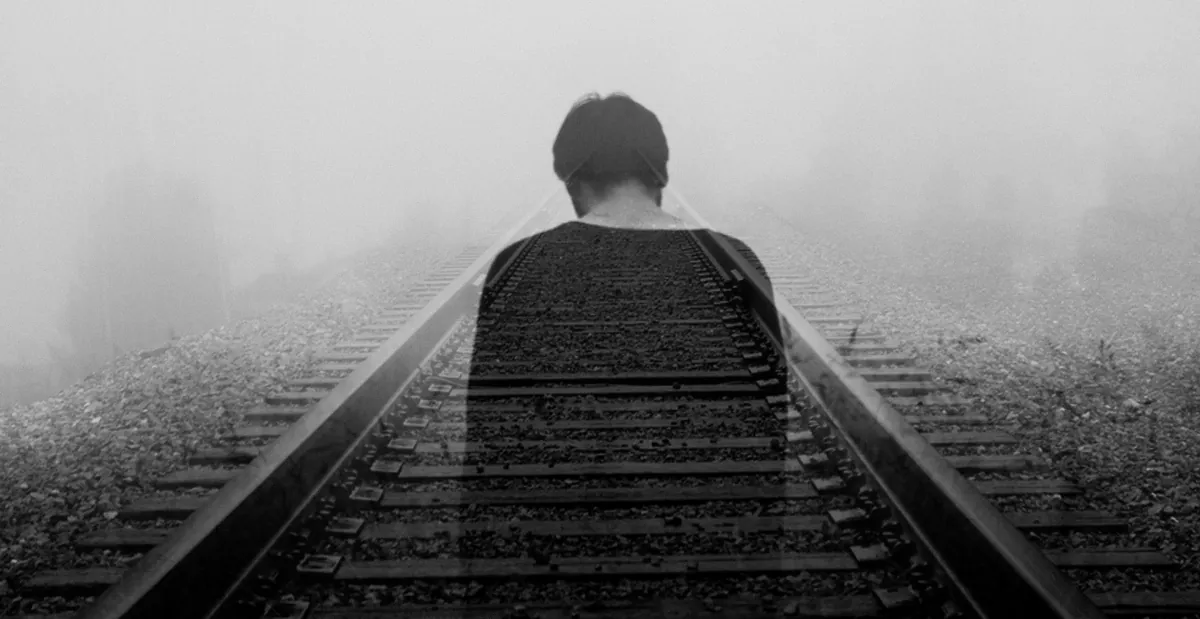Double exposure of a person fading into foggy railway tracks, symbolising feelings of loss, emptiness and depression in need of professional mental health support in Denmark