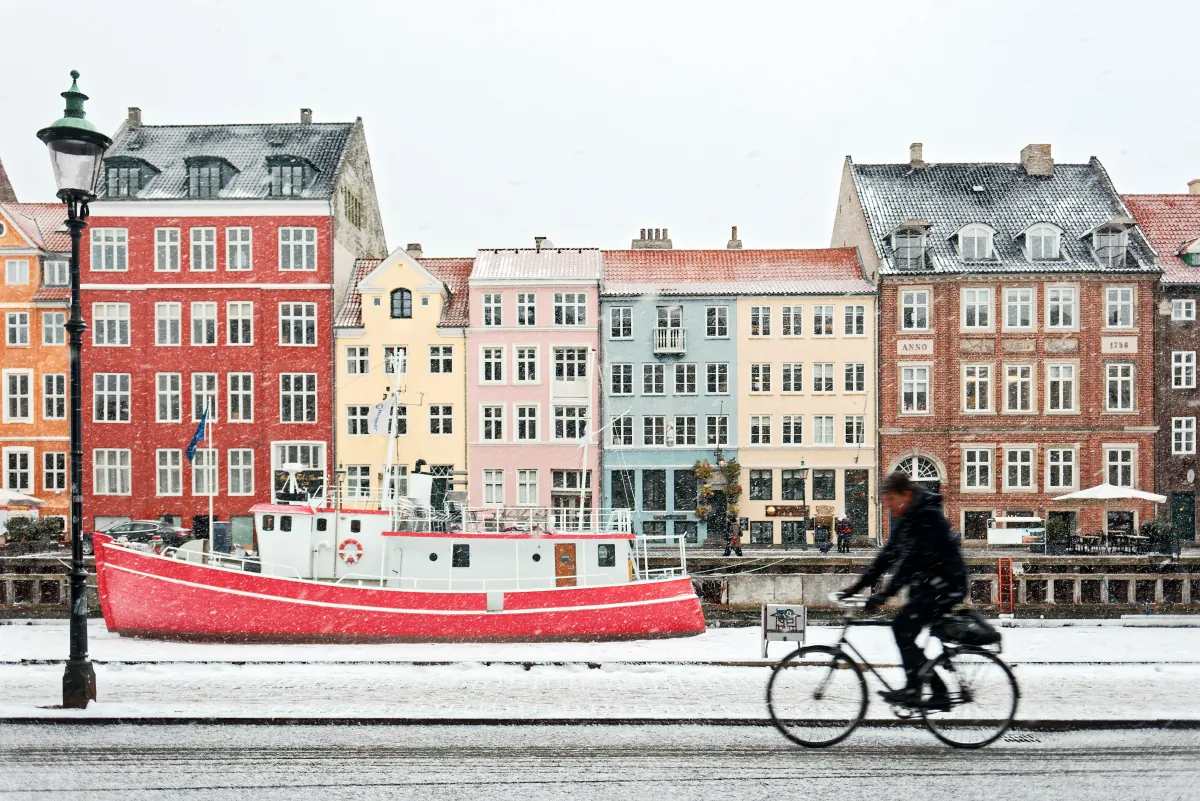 Cyclist passing the iconic colourful buildings of Nyhavn in Copenhagen during a snowy winter day, representing life as an expat in the Danish capital