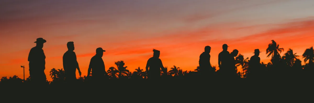 Silhouettes of a group of men standing together against a vivid sunset sky, symbolising male community, masculinity and the importance of men seeking mental health support
