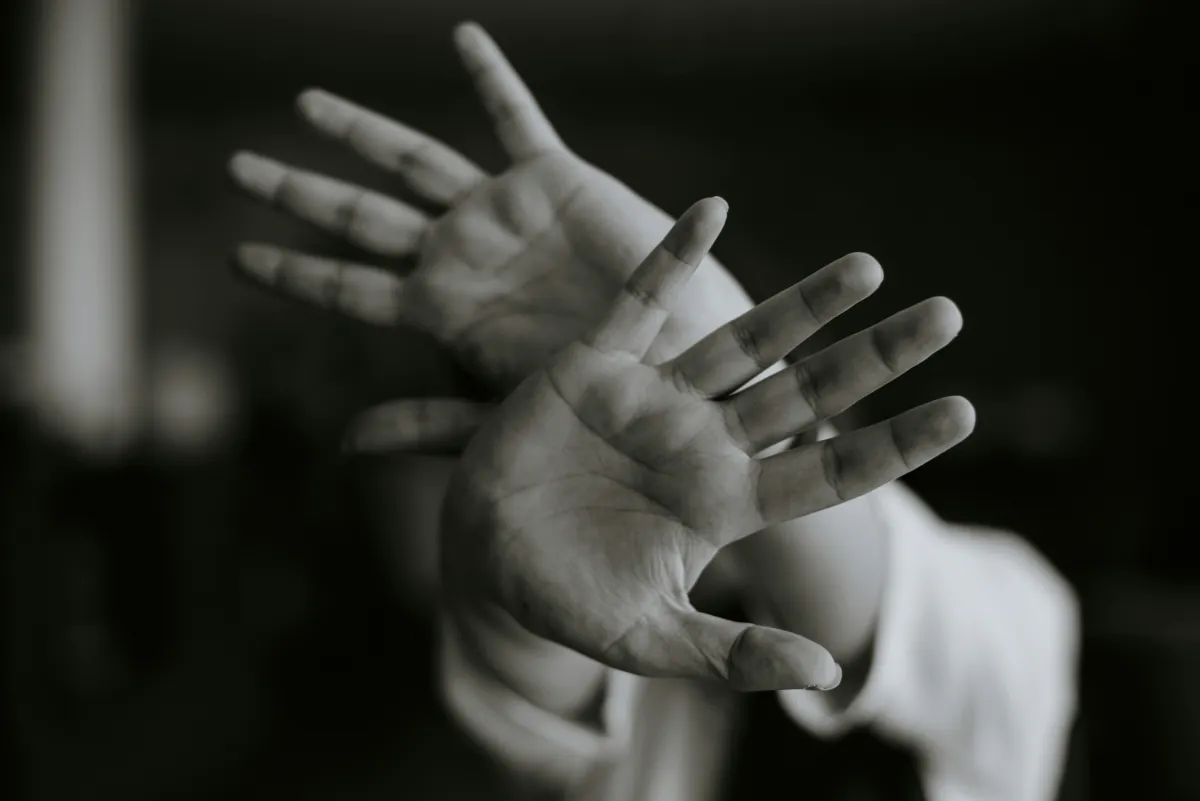 Person holding both hands up in a defensive gesture against a dark background, symbolising fear, panic and the overwhelming experience of living with phobias