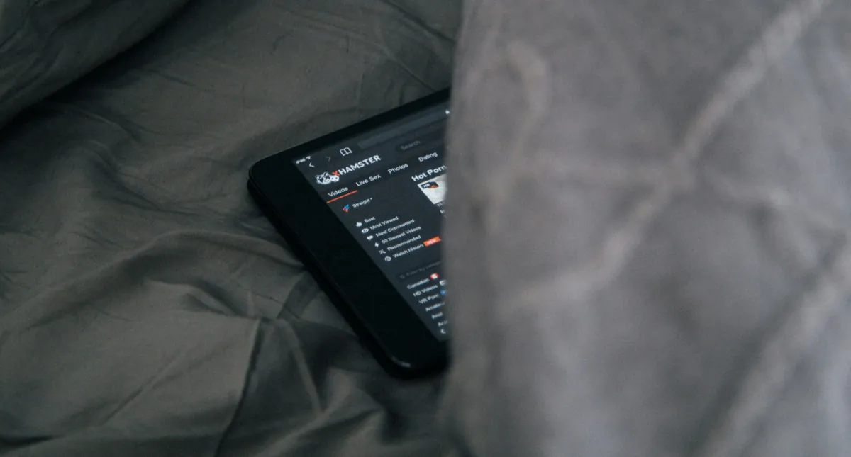 Smartphone hidden in bed sheets displaying an adult content website, symbolising secrecy, shame and the compulsive patterns of pornography addiction