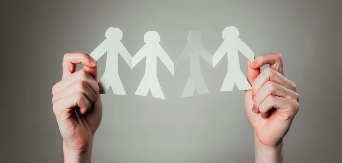 Hands holding a chain of paper people figures, symbolising the importance of human connection, relationships and community in mental health and wellbeing