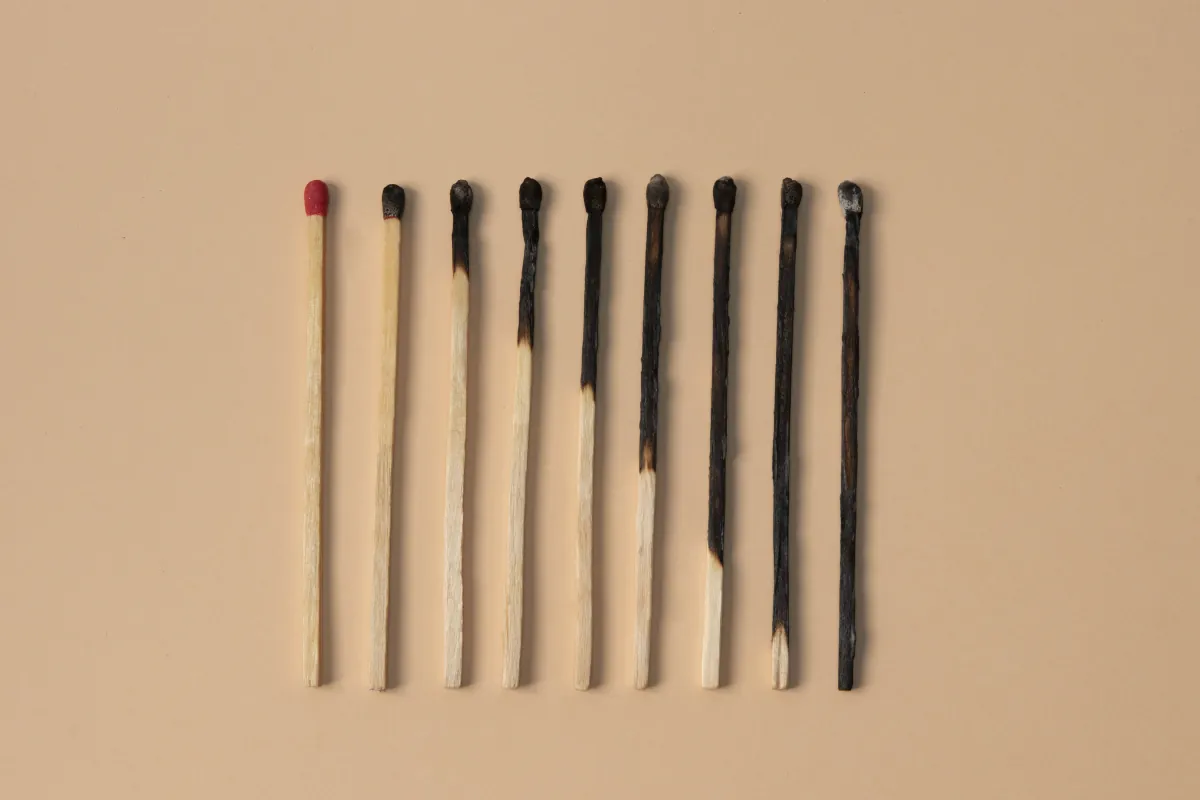 Row of matches in various stages of burning from intact to completely charred, symbolising the progressive stages of stress and burnout from full energy to total exhaustion